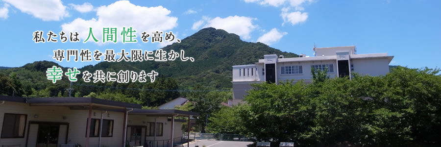 病院施設の外観と、その後方に緑の山々「私たちは人間性を高め、専門性を最大限に生かし、幸せを共に創ります」